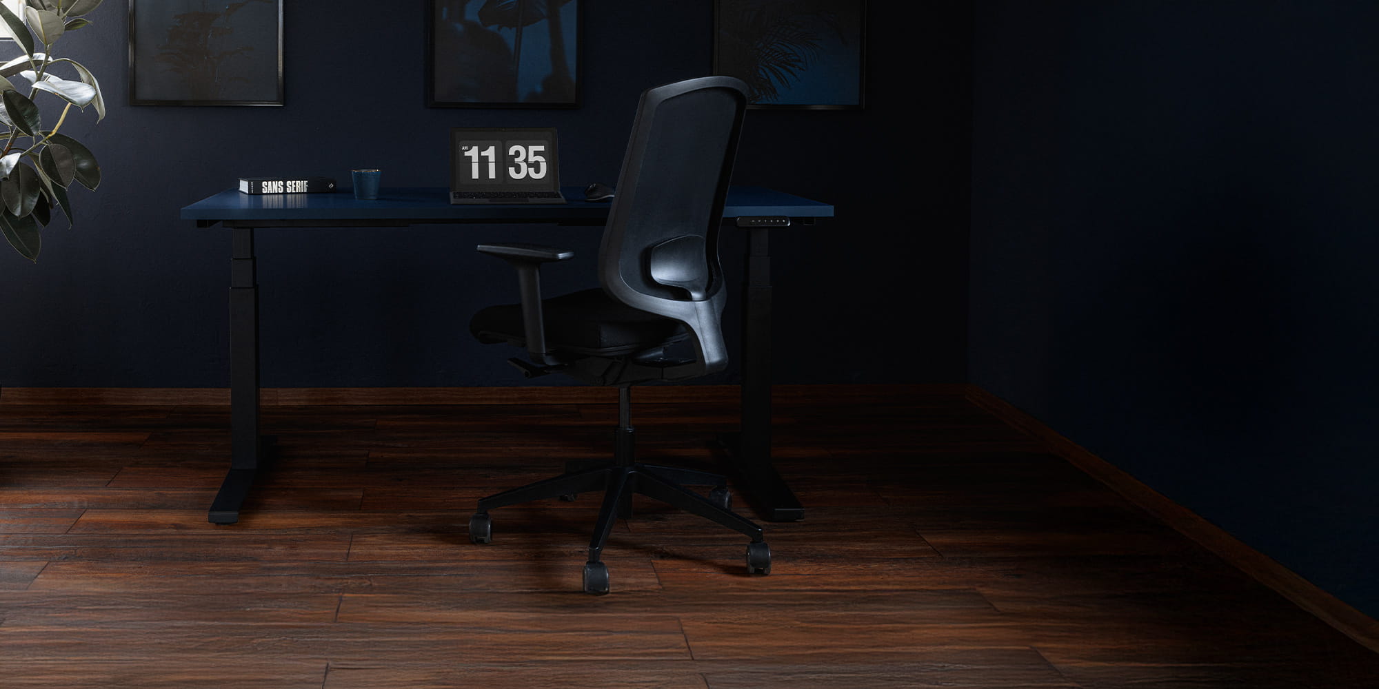 Modern desk with office chair and table clock ("11:35"), pictures on the wall and a plant in the room.