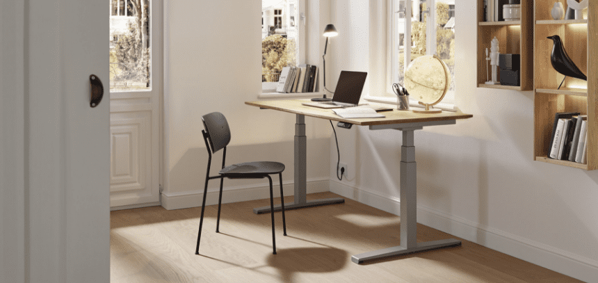 Moderner Schreibtisch mit Holzplatte und Stuhl, Laptop und Gegenstände auf dem Tisch, Regale und Fenster im Hintergrund.