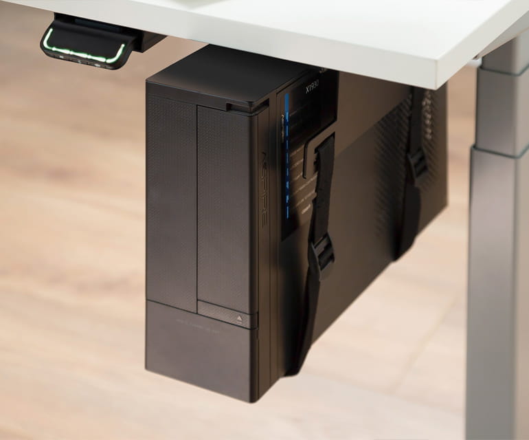 Bureau assis-debout moderne avec un plateau blanc, doté d’un support PC monté sous le bureau fixant solidement un ordinateur de bureau à l’aide de sangles.