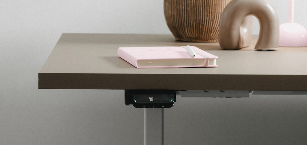Height-adjustable desk with control panel, with a notebook, pen, and decorative objects on it.