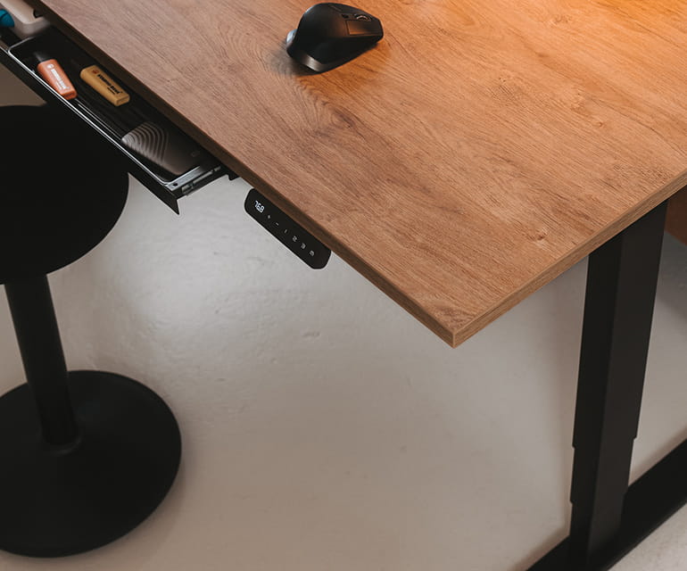 Höhenverstellbarer Schreibtisch mit Holzplatte und schwarzem Gestell, ausgestattet mit einer ausziehbaren Schublade, einem digitalen Bedienfeld und einer Maus, dazu ein ergonomischer Hocker.