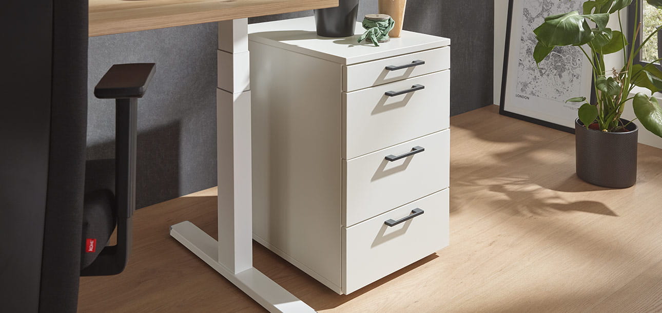 Cabinet roulant blanc avec trois tiroirs au bureau, plantes et cadre photo en arrière-plan.