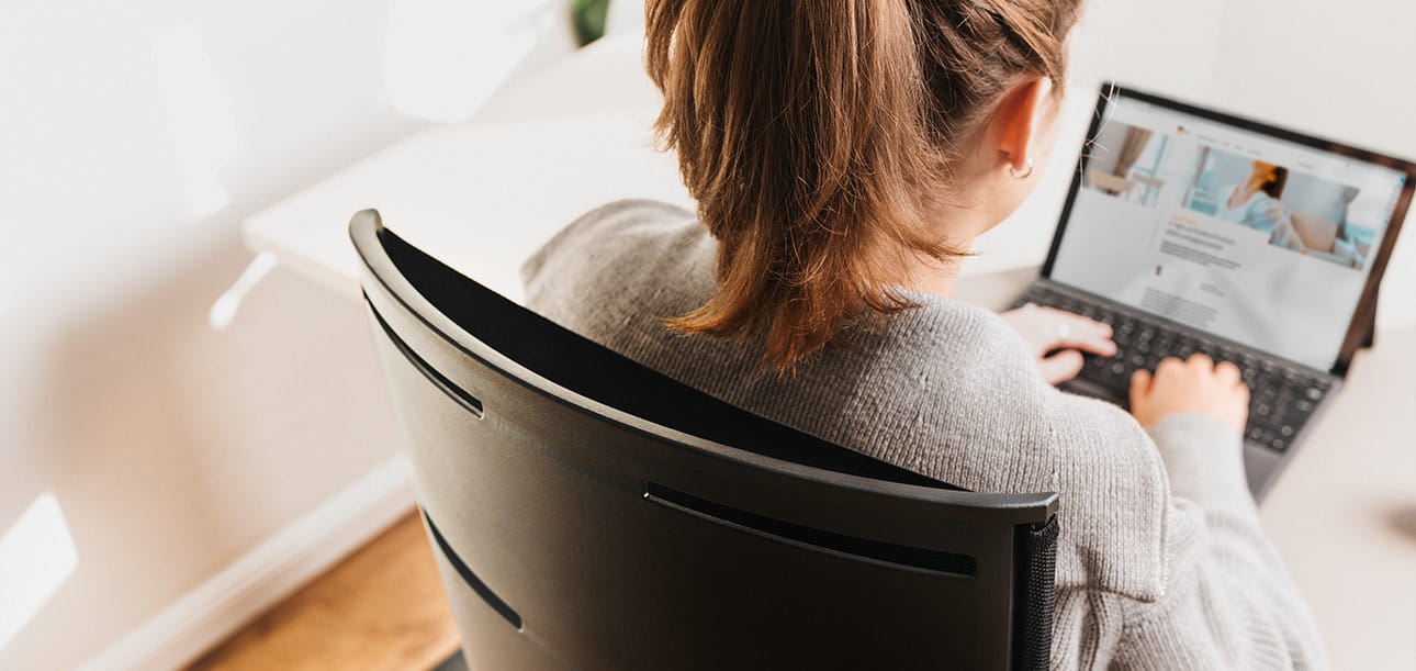 Person sitting at a desk working on a laptop, view from behind looking at the screen.