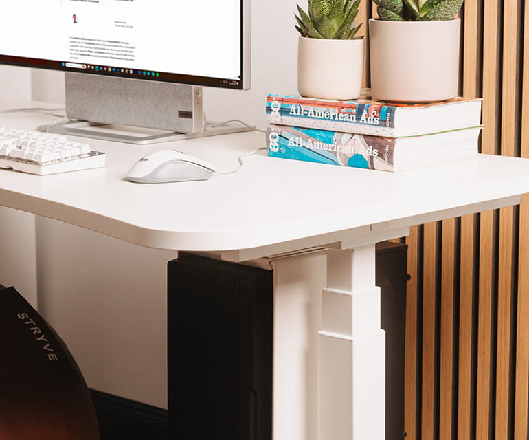 Im Homeoffice mit Eiche-Wandpaneel steht ein weißer Schreibtisch. Die weiße Tischplatte hat eine abgerundete Kante. Es steht ein Monitor auf der Schreibtischplatte, eine Tastatur und Bücher liegen ebenfalls darauf. Ein brauner Sitzball liegt unter dem Sch