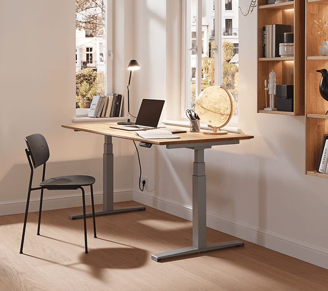 Height-adjustable desk with laptop, lamp, globe, and black chair in a sunny room with a shelf.