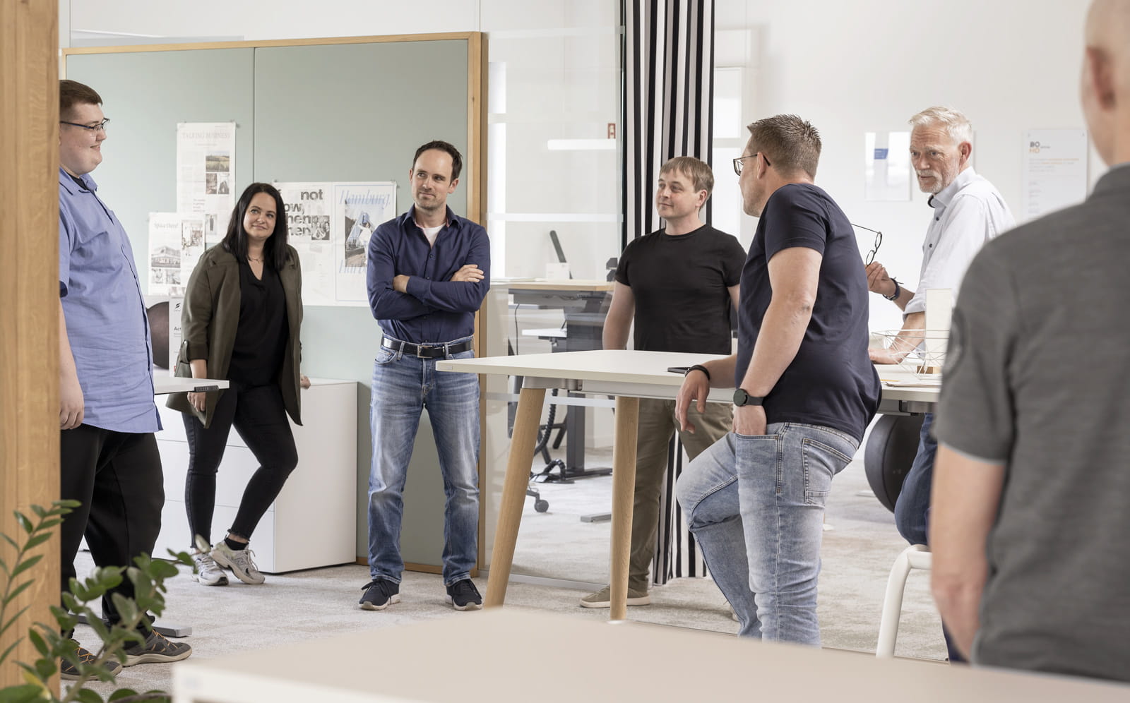 Sechs Personen stehen in einem modernen, hellen Büro und unterhalten sich an einem hohen Besprechungstisch.