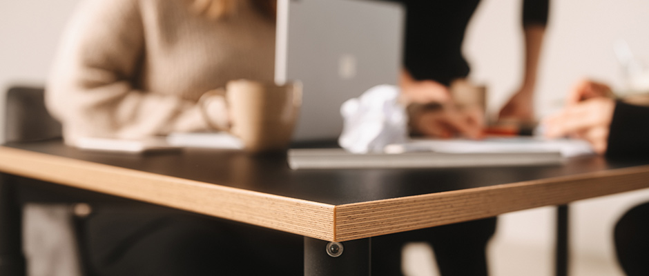 Zwei Personen sitzen an einem Tisch mit einem Laptop, Tassen und Unterlagen, während sie gemeinsam arbeiten.