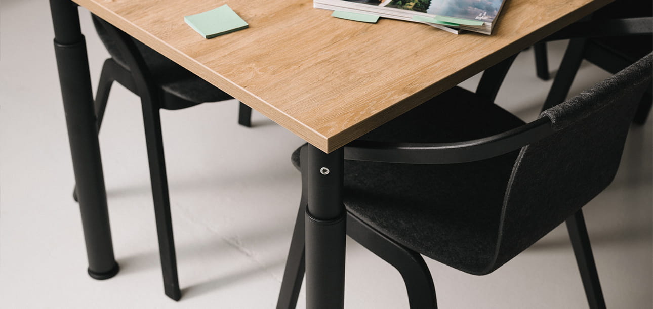 Konferenztisch mit Holzplatte, schwarze Stühle darum, Notizzettel und ein Magazin auf dem Tisch.