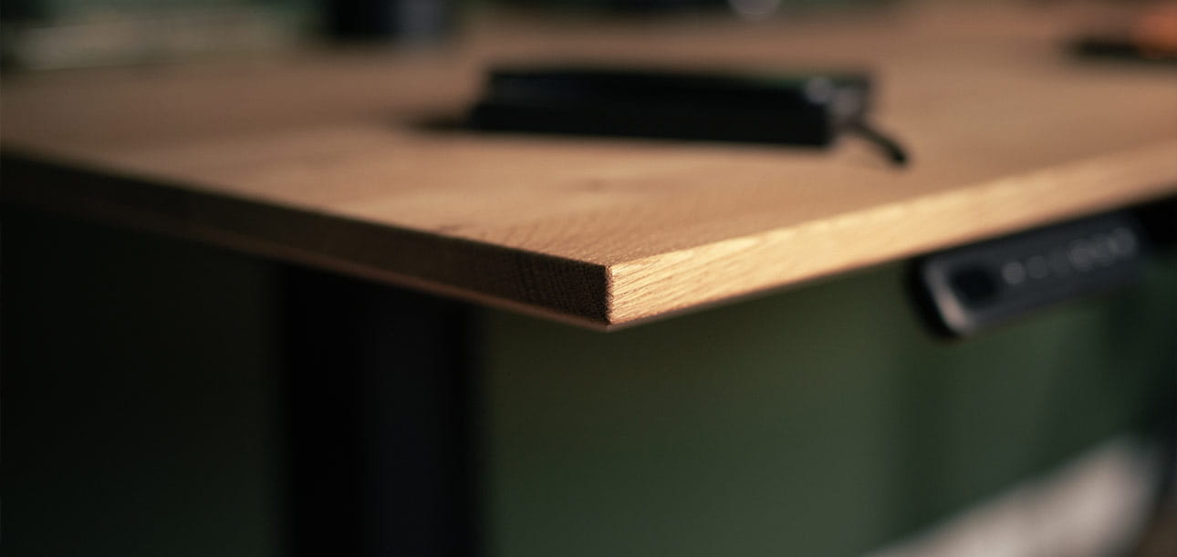 Wooden desk edge with control panel for height adjustment underneath, black object on the desk.