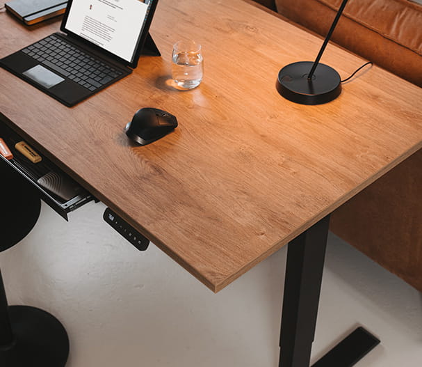 Höhenverstellbarer Holztisch mit Laptop, Maus und Lampe. Bedienelement für die Höhenverstellung unter dem Tisch.