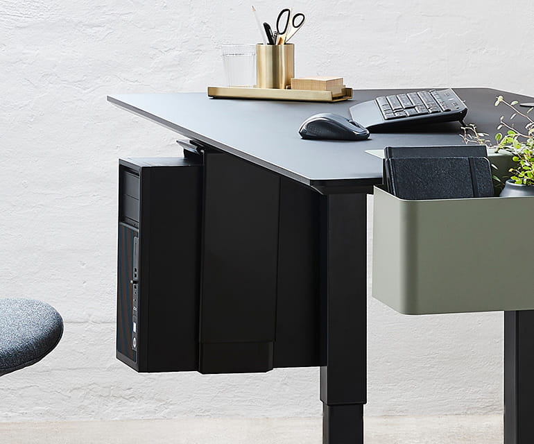 Bureau assis-debout moderne avec un plateau noir, doté d’un support PC monté sur le côté et d’un bac de rangement.