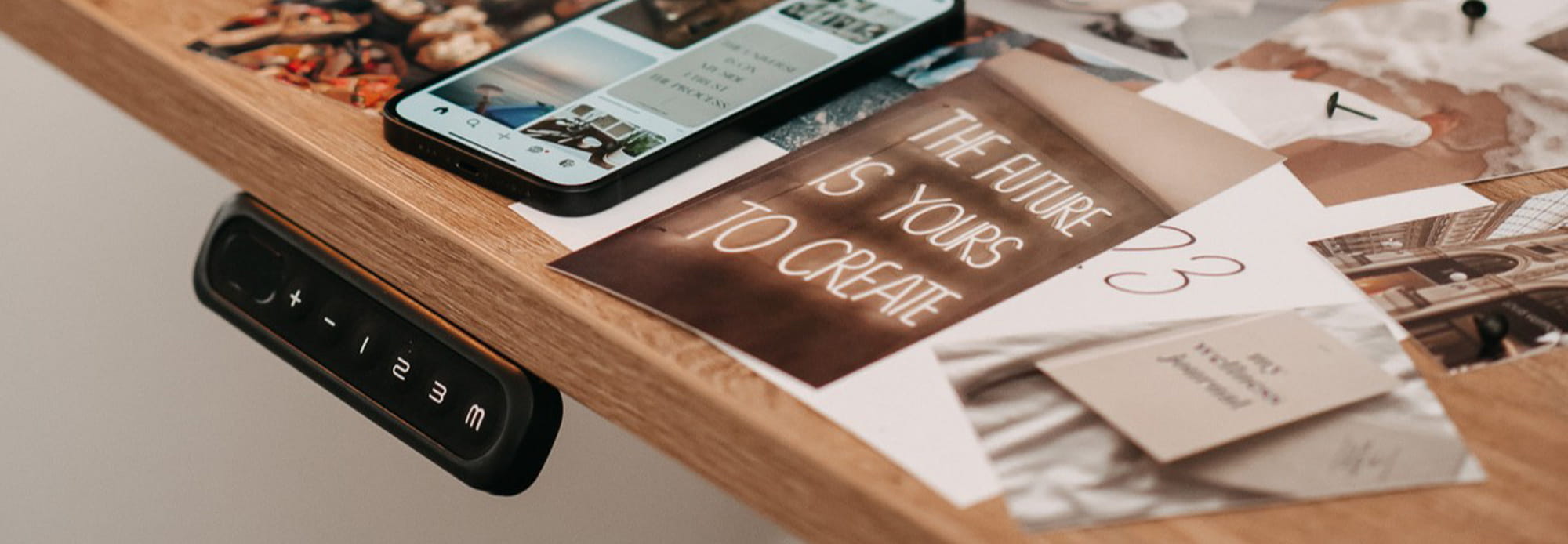 Height-adjustable desk with control panel, with photos and a smartphone displaying inspiring quotes and images. Wooden desk top.